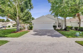 Single-story residence featuring a white exterior, attached garage, and a paver driveway
