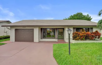 Single-story residence featuring a brown garage door, front entry, landscaped shrubbery, and a paved driveway