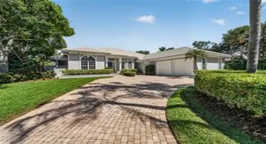 Paved driveway, manicured lawn, lush landscaping, arched windows, and a two-car side entry garage
