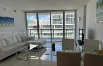 Floor-to-ceiling sliding glass doors opening to a balcony with metal railing, reflective tile flooring, and neutral wall finishes