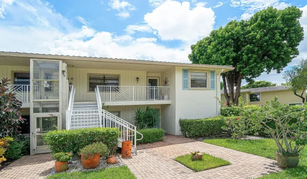 Brick paver walkway, lush landscaping, covered balcony, exterior elevator, and mature trees