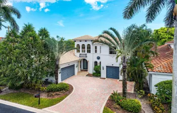 Mediterranean-inspired architecture, modern color palette, with a barrel tile roof, arched windows, a paver driveway, and mature landscaping