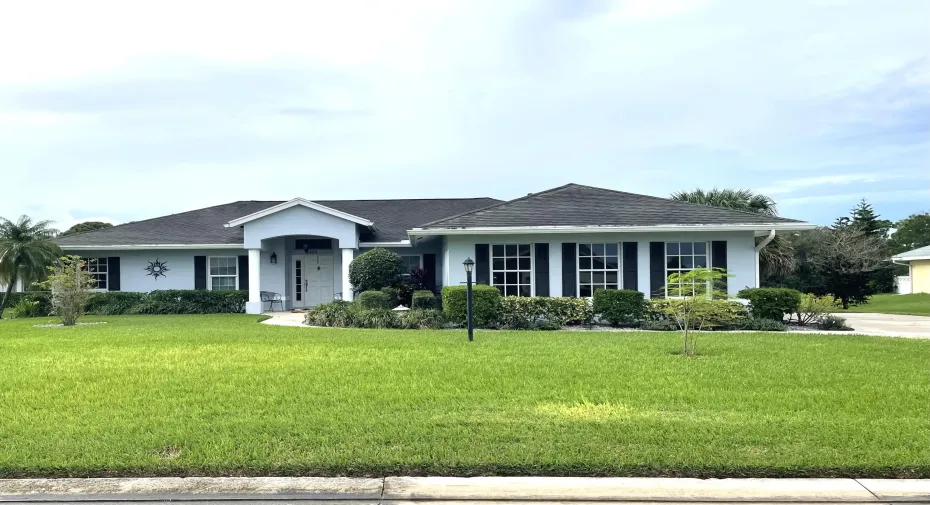 Exterior featuring a light blue facade, dark roof, prominent entryway with white columns, shuttered windows, and a landscaped front yard