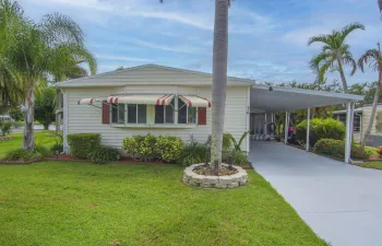 White siding exterior with a carport, bay window, and striped awning