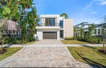 Modern two-story architectural exterior featuring smooth stucco siding, an upper-level balcony with horizontal metal railings, a paver driveway, and an integrated two-car garage