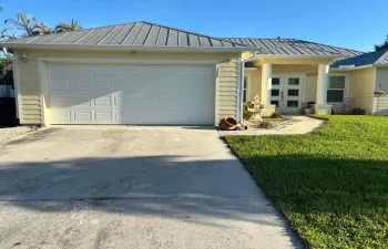 Front exterior with a metal roof, light-colored siding, an attached garage, a concrete driveway, and a paved walkway leading to the entry
