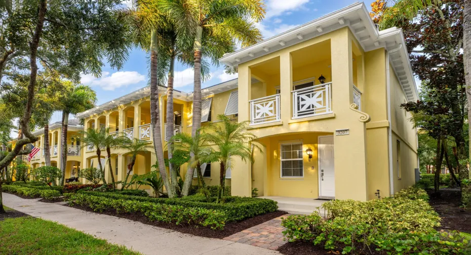 Stucco exterior featuring multiple balconies, decorative white railings, lush landscaping, and a brick paver walkway