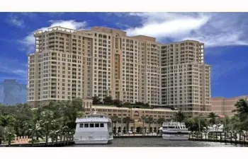 Multi-story building with multiple balconies, a waterside location, and surrounding mature trees