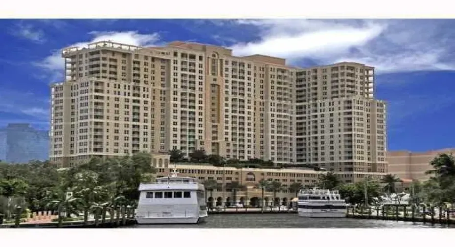 Multi-story building with multiple balconies, a waterside location, and surrounding mature trees