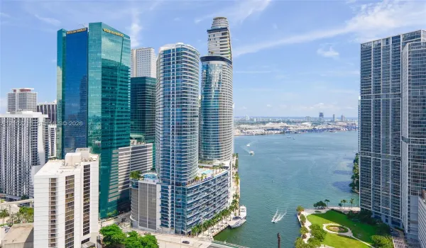 Urban high-rise exterior featuring a glass-curtain facade, balcony tiers, integrated podium parking, and proximity to a coastal waterway