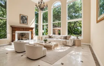 Soaring ceilings, arched windows, carved wood fireplace mantel, marble tile flooring with contrasting accents, and a tiered chandelier