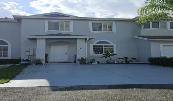 Two-story stucco exterior with white-framed windows, a covered entry, and a paved driveway