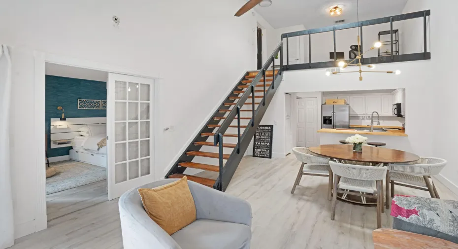 Open-concept living area with high ceilings, wood-finish flooring, a loft space, and a modern kitchen featuring white cabinetry and wood countertops