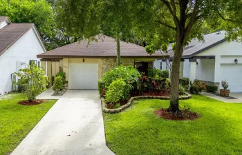 Single-story residence featuring a paved driveway, attached garage, stone veneer facade, mature trees, and landscaped grounds