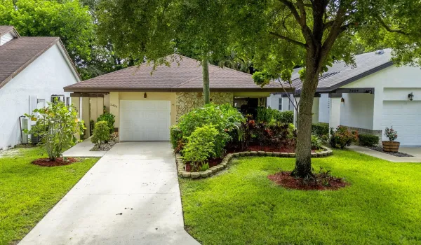 Single-story residence featuring a paved driveway, attached garage, stone veneer facade, mature trees, and landscaped grounds