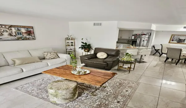 Open-concept living space with tile flooring throughout, a kitchen island with seating, white cabinetry, and stainless steel appliances