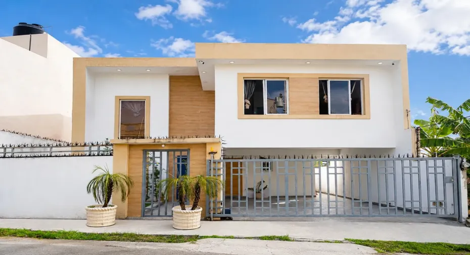 Contemporary two-story exterior with a two-tone facade, featuring multiple windows, and an integrated carport behind a metal gate