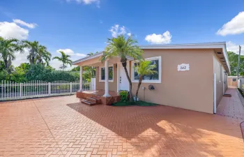 A welcoming front porch, tropical palms, and a broad paved frontage introduce this Hialeah home.