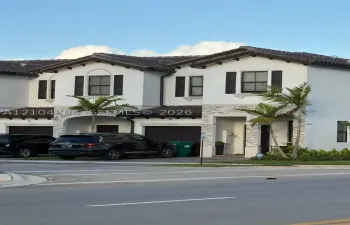 Stucco exterior featuring dual-gable rooflines, decorative stone-veneer accents, dark-toned tile roofing, and integrated garage doors