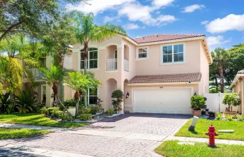Stucco exterior with a tile roof, paver driveway, integrated two-car garage, and established landscaping