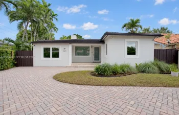 Single-story residence featuring a smooth stucco exterior, herringbone-pattern paver driveway, covered front entryway, and mature landscaping