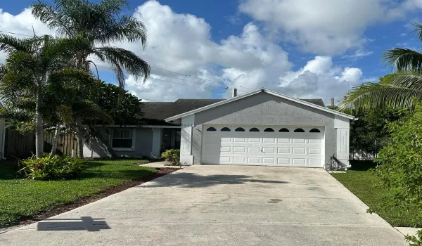 Exterior featuring a gabled roofline, attached garage with decorative windows, concrete driveway, mature landscaping, and a fenced yard