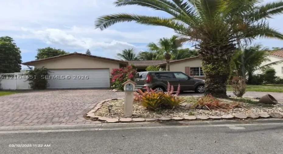 Paved brick driveway, attached two-car garage, mature palm trees, and established landscaping