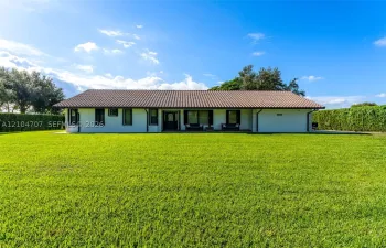 Single-story residence featuring a low-pitched tiled roof, light-toned exterior finish, and an expansive manicured lawn bordered by mature hedge fencing