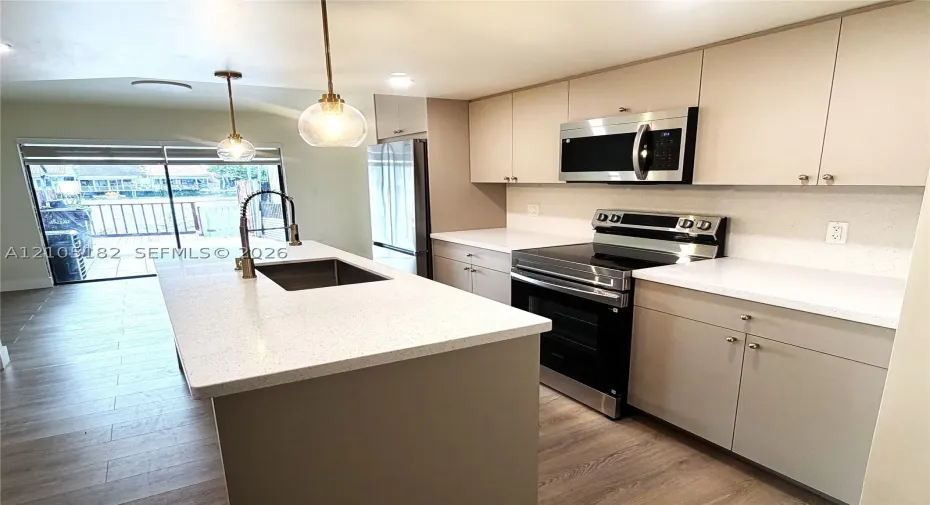 Kitchen featuring a center island with an undermount sink, pendant lighting, wood-finish flooring, white countertops, and stainless steel appliances