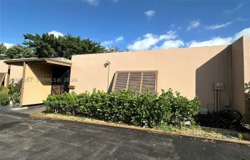 Stucco exterior with an attached awning, security gate, and mature perimeter landscaping