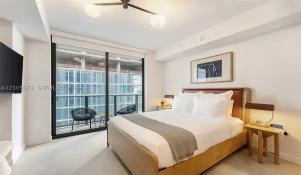 White walls, a ceiling-mounted light fixture, and a sliding glass door opening to a private balcony with metal railings