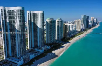 Coastal high-rise residences with private balconies, set along a sandy beach and turquoise waters