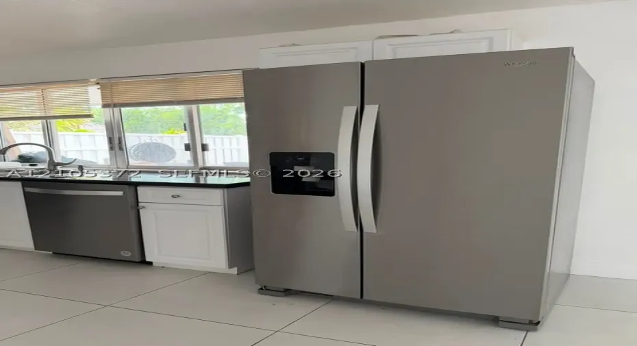 Stainless steel side-by-side refrigerator, stainless steel dishwasher, white cabinetry, dark stone countertop, and tile flooring