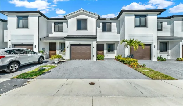 Modern exterior with white stucco finish and dark trim, featuring paver driveways, attached garages, and established landscaping