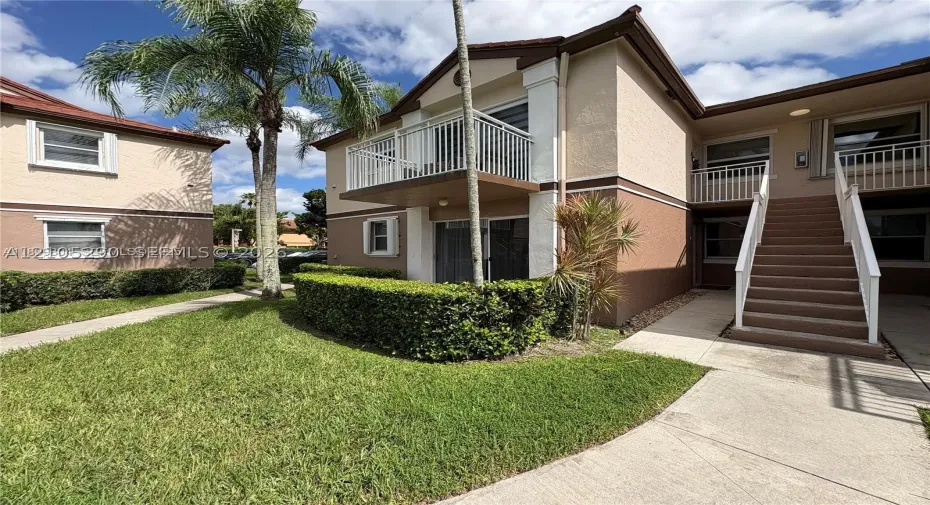 Two-tone exterior with stucco finish, private balcony, exterior staircase, and manicured landscaping