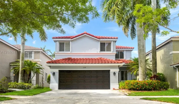 Two-story stucco exterior with a red barrel tile roof, integrated garage, and manicured landscaping