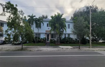Two-story building with light blue exterior, prominent palm trees, and mature landscaping