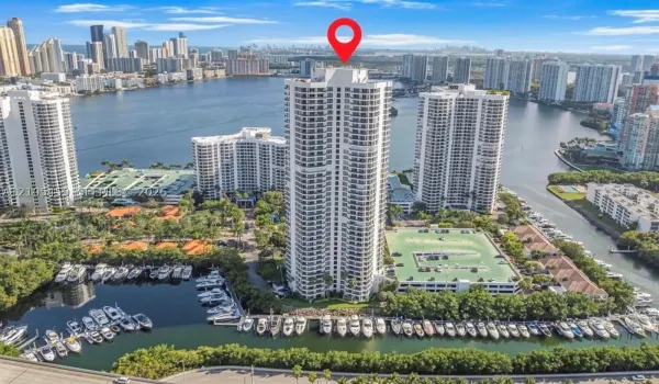 Waterfront high-rise building with multiple balconies, adjacent to a marina with numerous boats