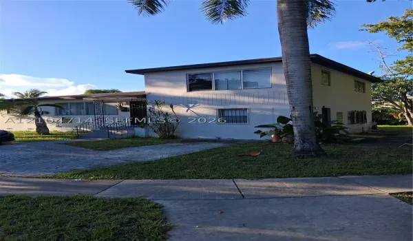 Two-story white stucco exterior with multiple windows, a prominent palm tree, and a concrete paver driveway