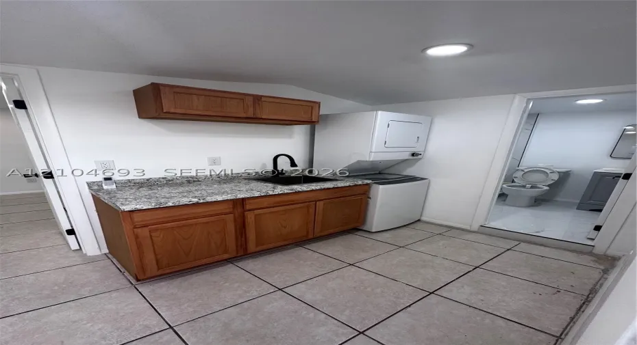 Utility area featuring a granite-finish countertop, wood cabinetry, a black sink with a gooseneck faucet, and a tile floor
