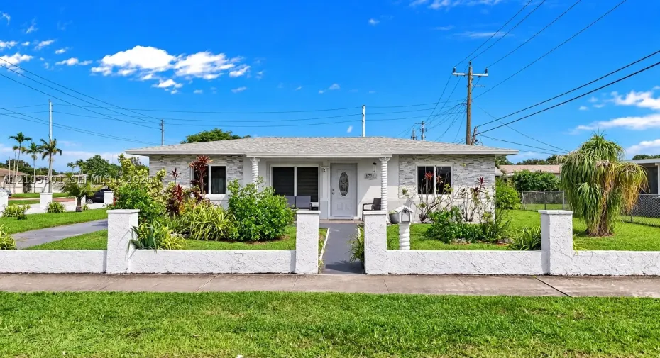 White exterior with stone-finish accents, a paved driveway, mature landscaping, and a low privacy wall