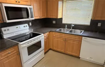 Kitchen featuring wood cabinetry, dark countertops, a double-basin stainless steel sink, a white electric range, and an over-the-range microwave
