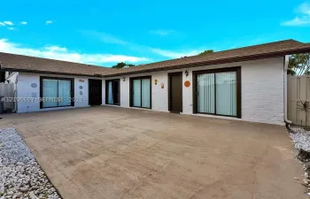 White brick exterior with a brown shingle roof, dark-framed sliding glass doors, and a concrete patio