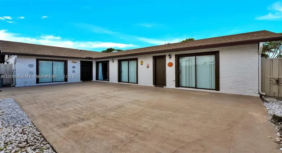 White brick exterior with a brown shingle roof, dark-framed sliding glass doors, and a concrete patio