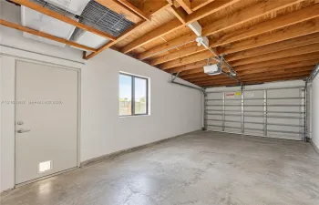 Concrete flooring, exposed wood beam ceiling, single window, overhead garage door with opener, and side entry door
