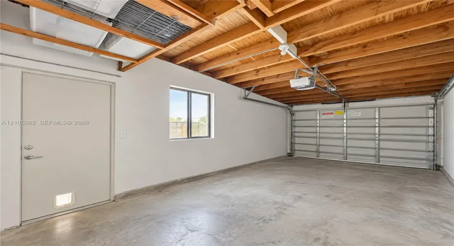 Concrete flooring, exposed wood beam ceiling, single window, overhead garage door with opener, and side entry door