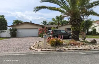 Paved brick driveway, attached two-car garage, mature palm trees, and established landscaping