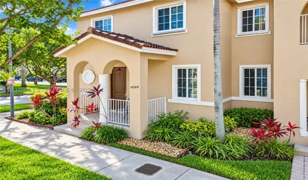 Stucco exterior featuring an arched covered entry, tiled gable roof, white metal railings, and multi-pane windows