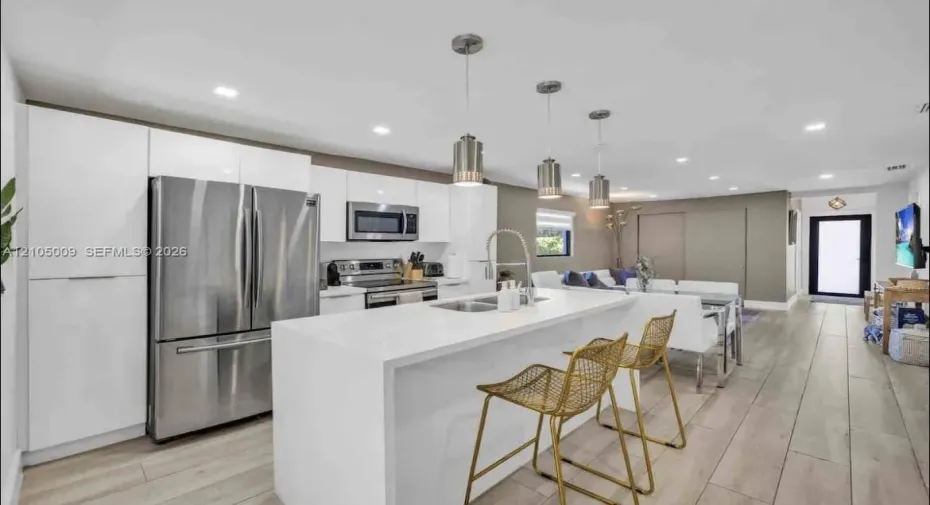 Modern kitchen featuring white cabinetry, stainless steel appliances, a center island with sink, and pendant lighting