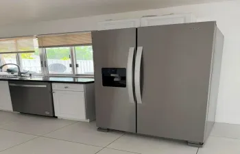 Stainless steel side-by-side refrigerator, stainless steel dishwasher, white cabinetry, dark stone countertop, and tile flooring